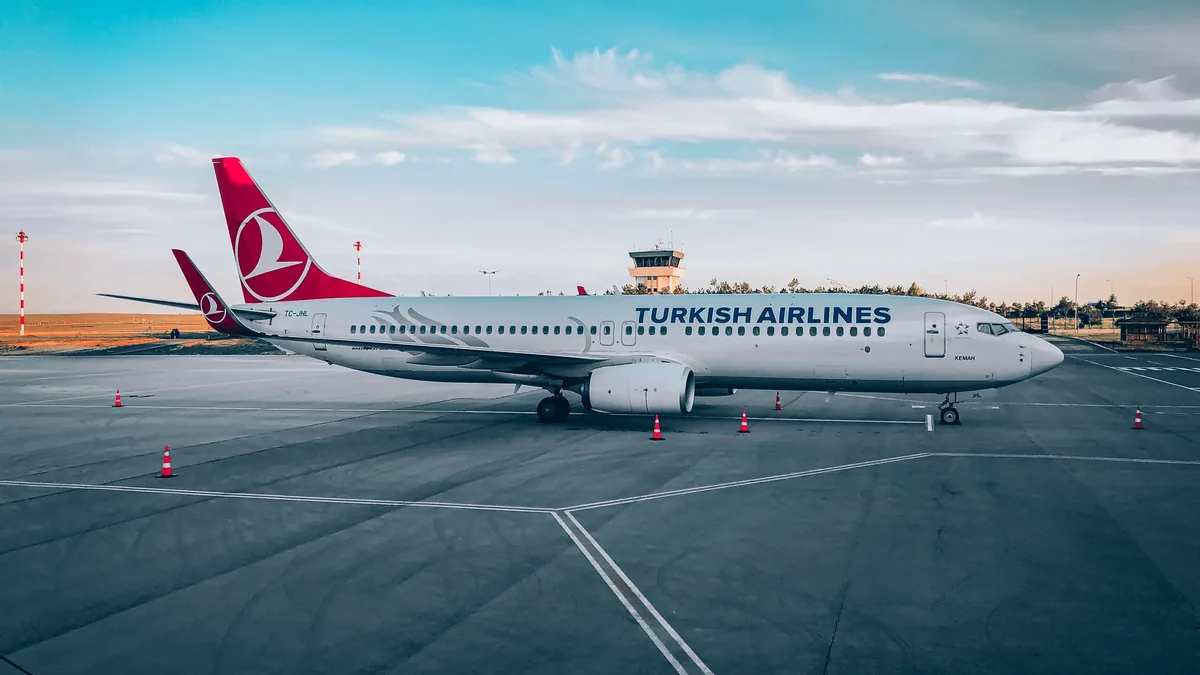 A Turkish Airlines plane parked on the tarmac at an airport, with a control tower visible in the background.